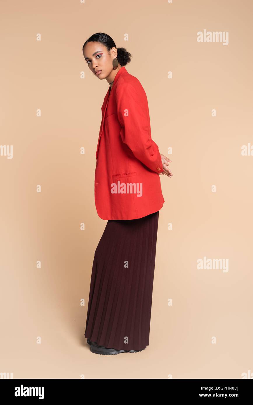 Elegantes afroamerikanisches Modell in breiter Hose und rotem Blazer in Beige, Stockbild Stockfoto