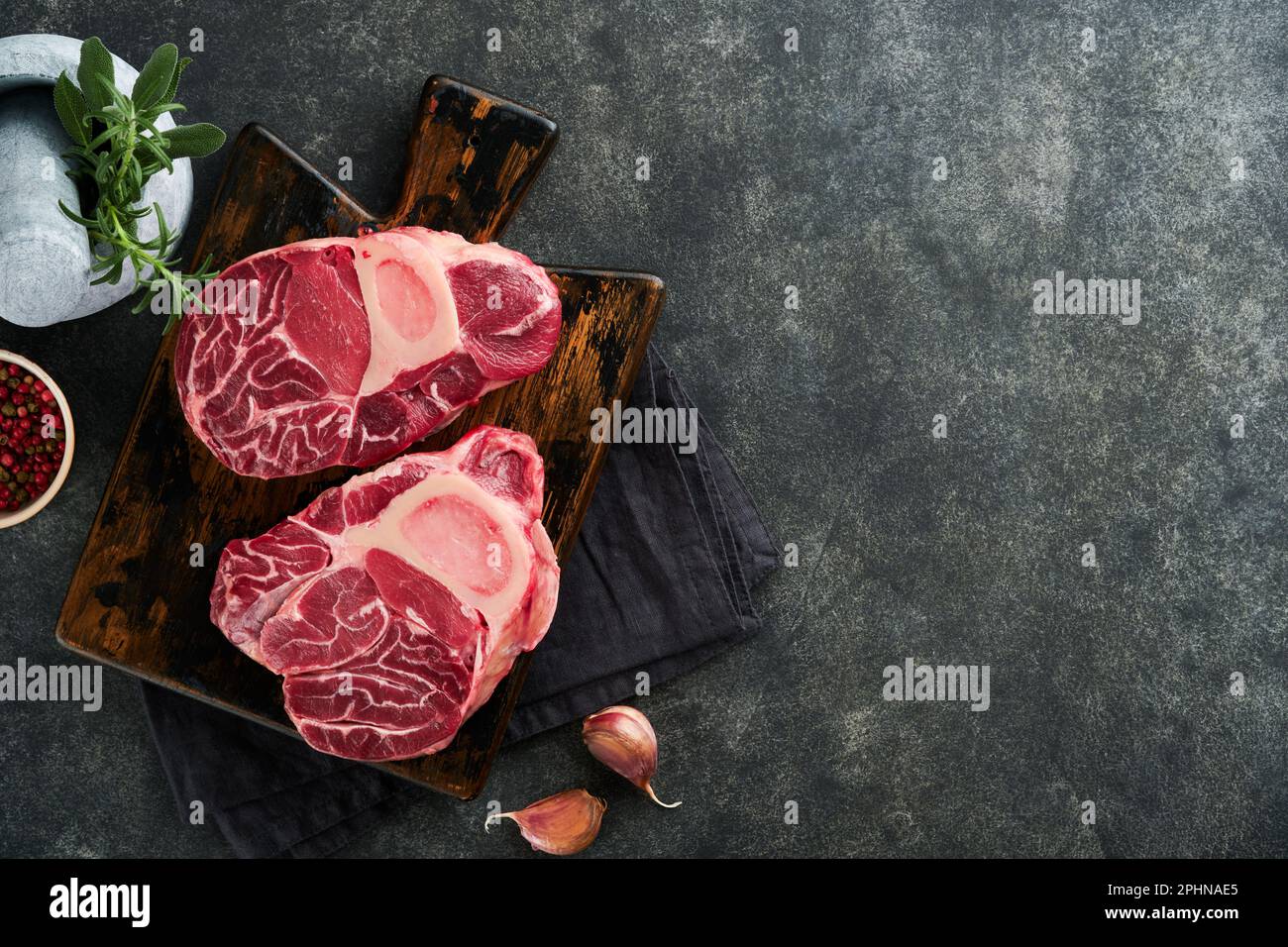 Rohes Steak-Fleisch von Osso Buco. Barbecue-Fleisch. Rohes, frisches, kreuzgeschnittenes Kalbsschenkel und Gewürze von Pfeffer, Rosmarin, Thymian und Salz auf dunklem Hintergrund. Rinderbein S Stockfoto