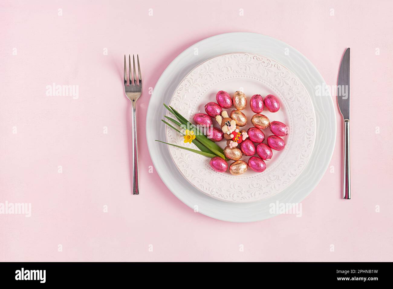 Frohe Ostern. Tischdecken für Osterferien. Ostereier, Kaninchen, Blumen und Besteck auf pinkfarbenem Hintergrund. Draufsicht, flach liegend Stockfoto