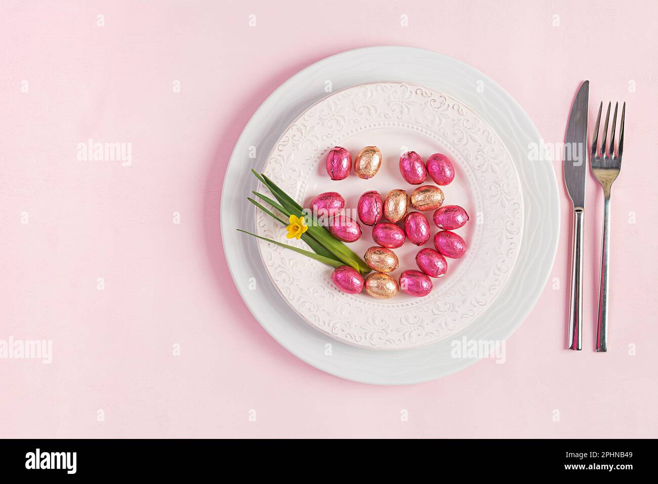 Frohe Ostern. Tischdecken für Osterferien. Ostereier, Blumen und Besteck auf pinkfarbenem Hintergrund. Draufsicht, flach liegend Stockfoto