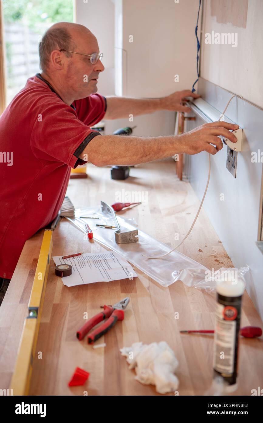 Küchenschlosser: Elektrische Installation. Ein Elektriker, der eine Lichtleiste auf einer neuen Küche installiert. Aus einer Reihe von zugehörigen Bildern. Stockfoto