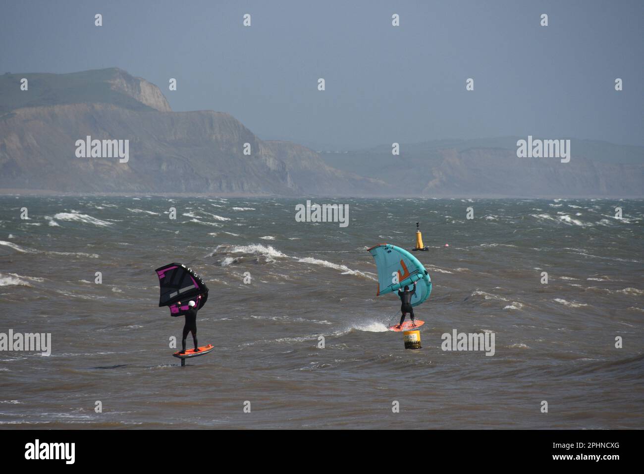 Ein paar Wing-Surfer gleiten durch ein zerklüftetes Meer, angetrieben von einer steifen Brise vor der Jurrasic Coast in Lyme Bay. Dorset.UK Stockfoto