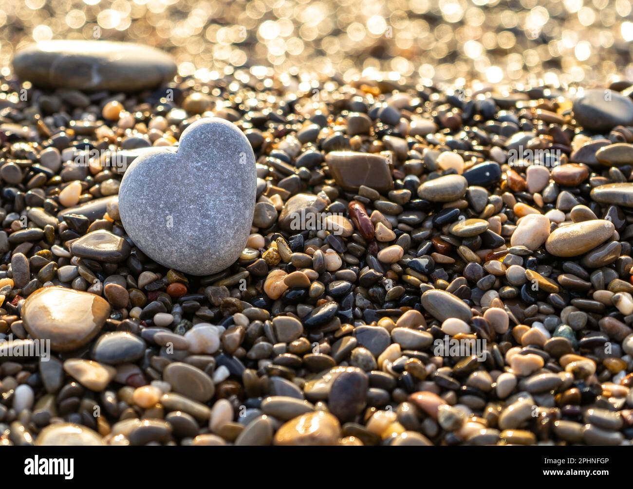 Stone Heart am Pebble Beach, Shining Ocean Water, Rocky Shore Love Symbol, Summer Pebble Heart, Urlaubskonzept, verschwommener Hintergrund Stockfoto