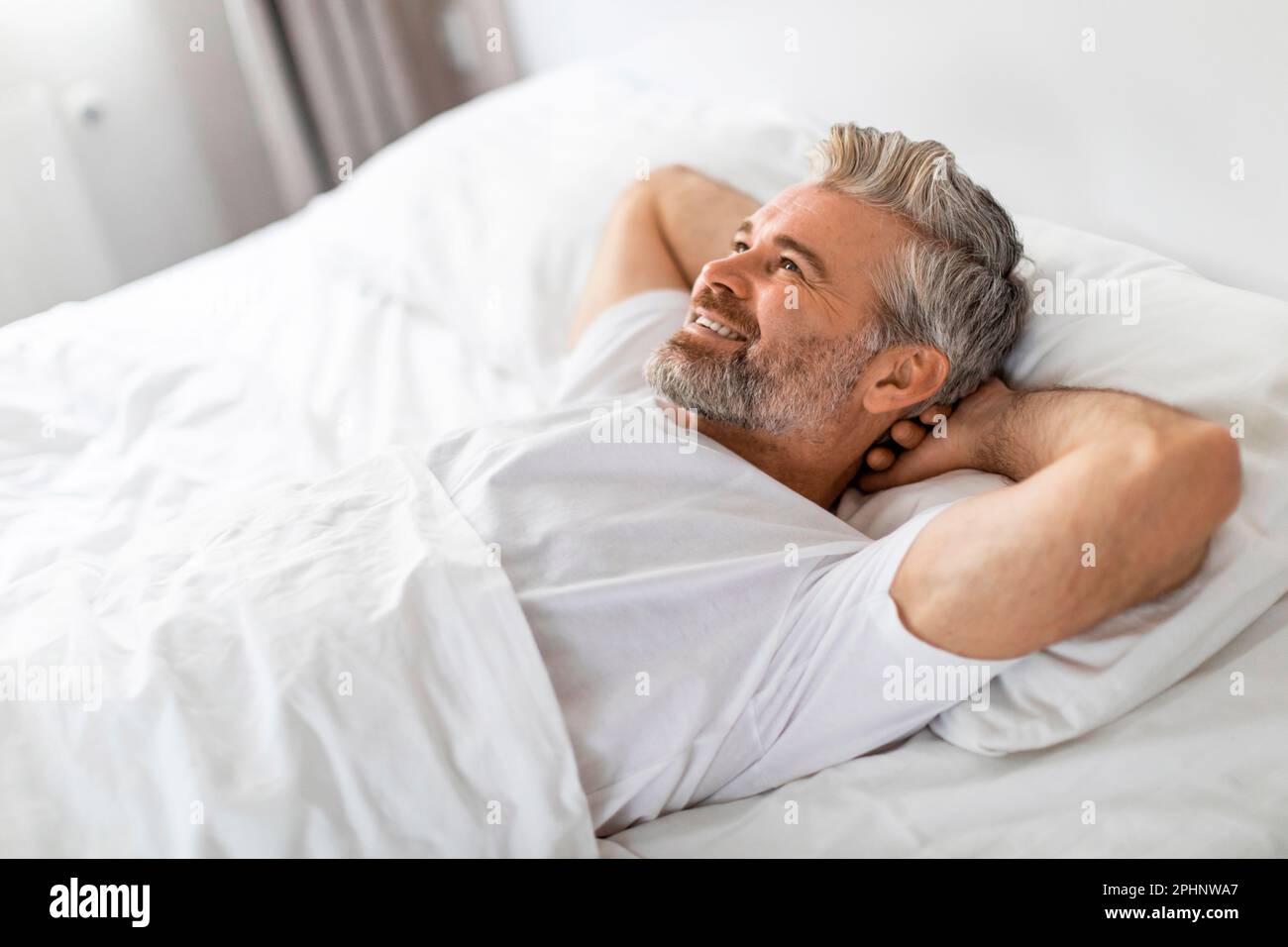 Gut ausgeruhter glücklicher Mann mittleren Alters, der sich im Bett entspannt Stockfoto