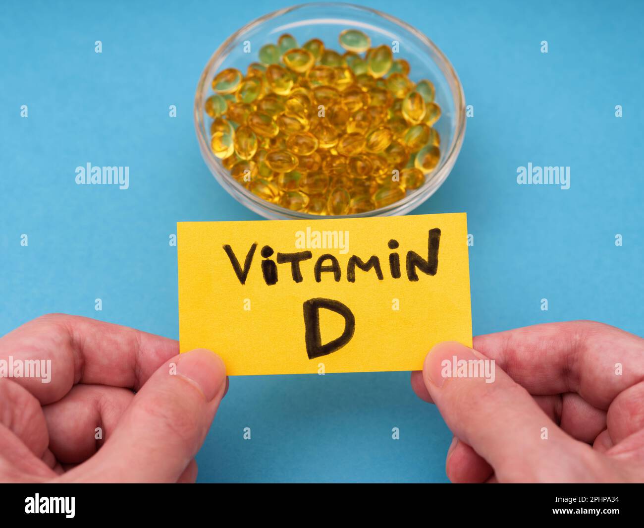 Ein Mann, der eine gelbe Papiernotiz mit den Worten Vitamin D in den Händen hält, über einer Glasschüssel mit Vitamin-D3-Softgels. Schließen. Stockfoto