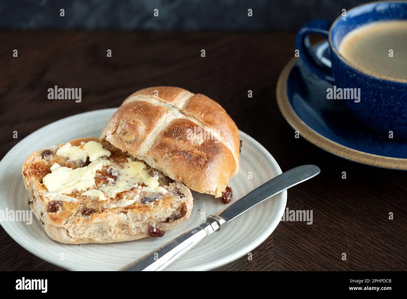Ein Osterbrötchen mit heißem Kreuz, getoastet und serviert mit Butter, die auf dem warmen Brötchen schmilzt. Traditionell am Karfreitag in Großbritannien serviert Stockfoto