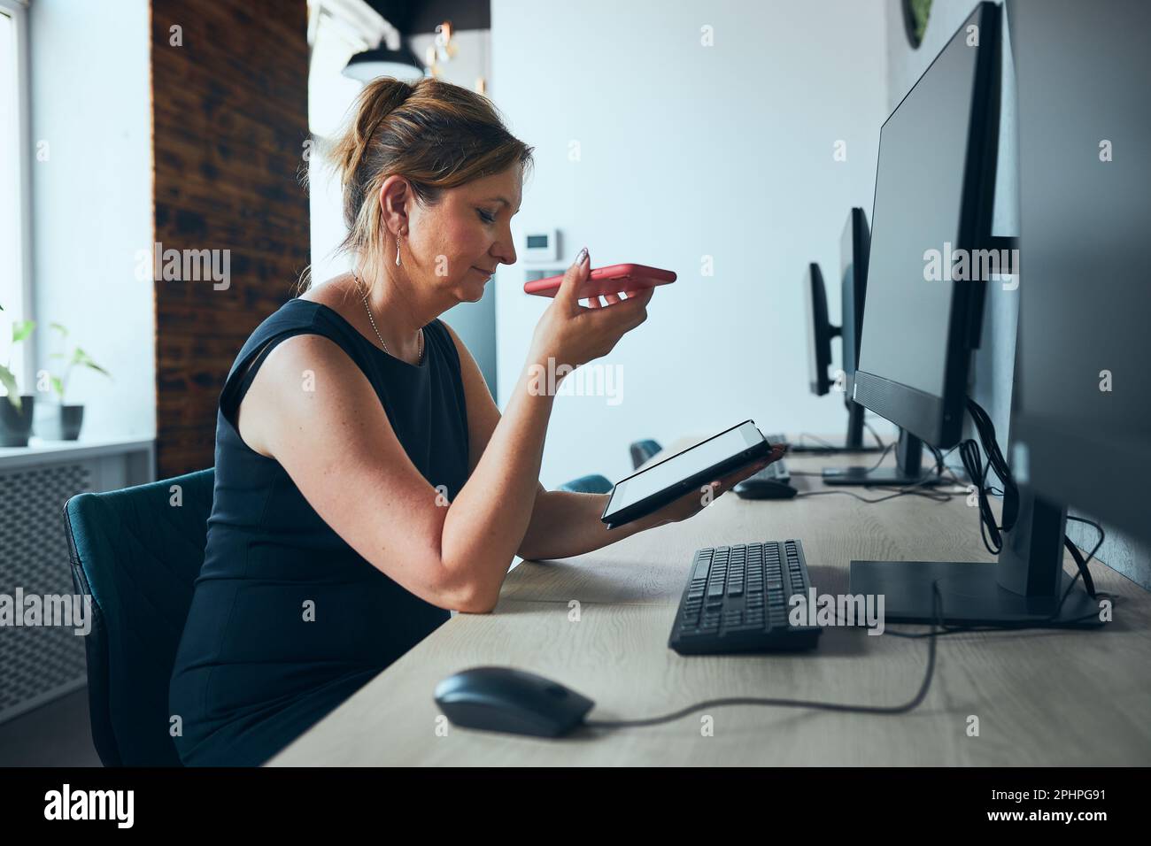 Geschäftsfrau mit Geschäftsanruf, die im Büro am Tablet arbeitet. Reife beschäftigte Frau mit Touchpad-Computer, der am Fenster in einem modernen Interieur steht. Fema Stockfoto