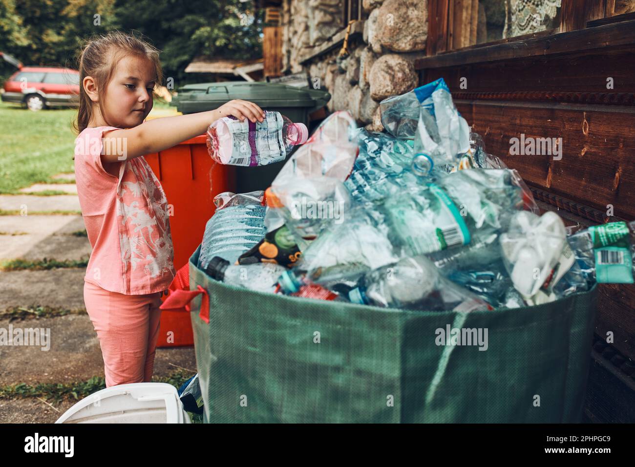 Kind kleines Mädchen werfen aus Plastikflasche zu großen Behälter voller Plastikmüll Stockfoto