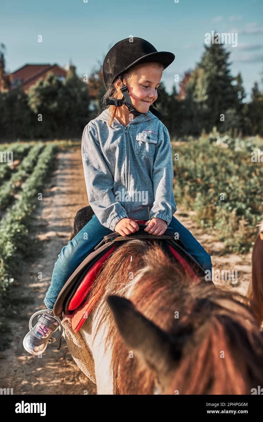 Kleines lächelndes Mädchen, das Reiten lernt. 5-6 Jahre alter Pferdesport im Helm mit Spaß Reiten ein Pferd Stockfoto