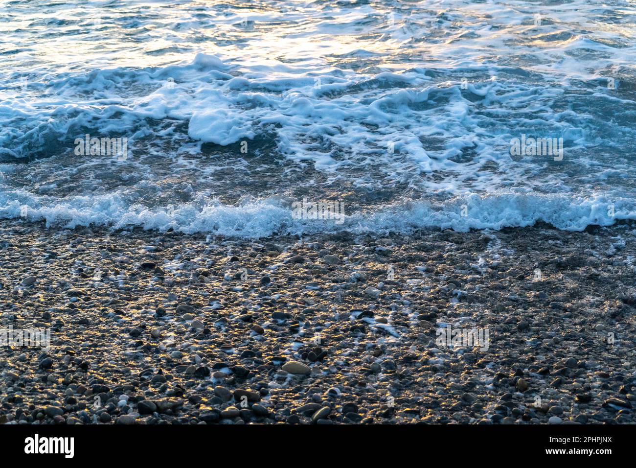 Meereswellen auf Kieselstrand-Texturhintergrund. Transparentes Meerwasser, felsiges Ufermuster, Sommermodell mit Kopierraum, Steinküste, Urlaub c Stockfoto