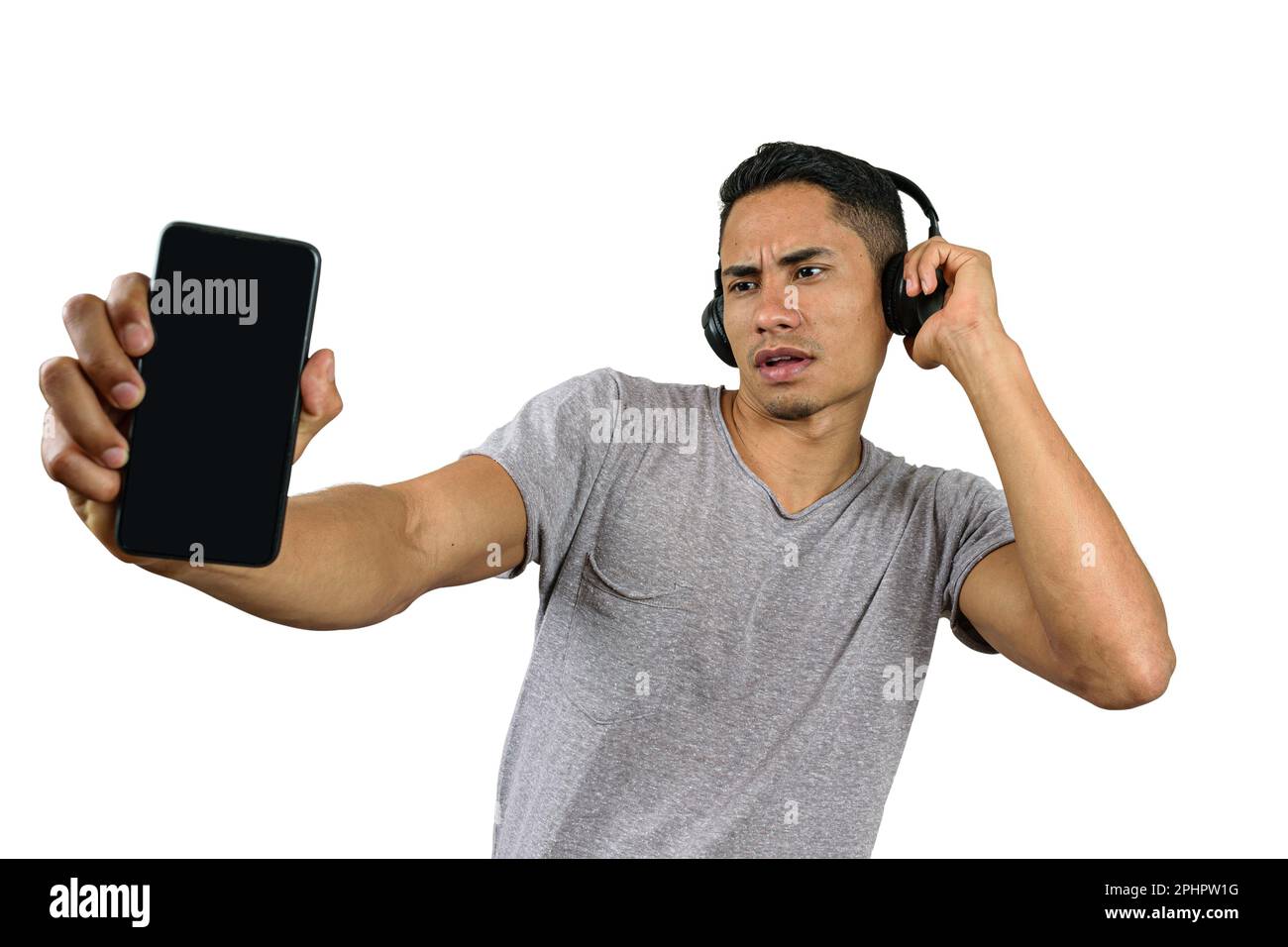 Der 28-jährige Brasilianer mit einer Hand auf dem kabellosen Kopfhörer schaute auf sein Smartphone und zeigte es der Kamera. Stockfoto