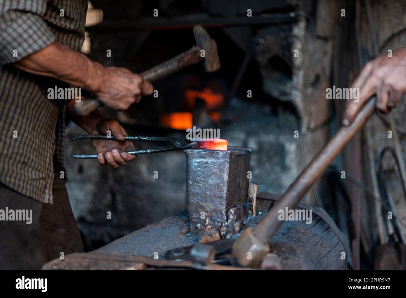Ein Schmied stellt in einer Werkstatt Eisenwerkzeuge mit Hammer her Stockfoto