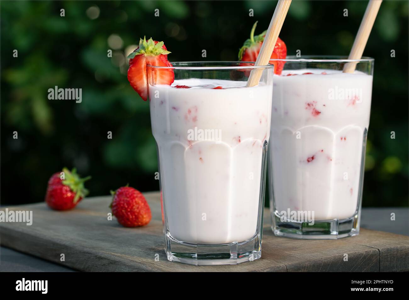 ErdbeerSmoothie in zwei Glasgläsern und frische Erdbeeren auf einem Holztisch im Hof. Stockfoto