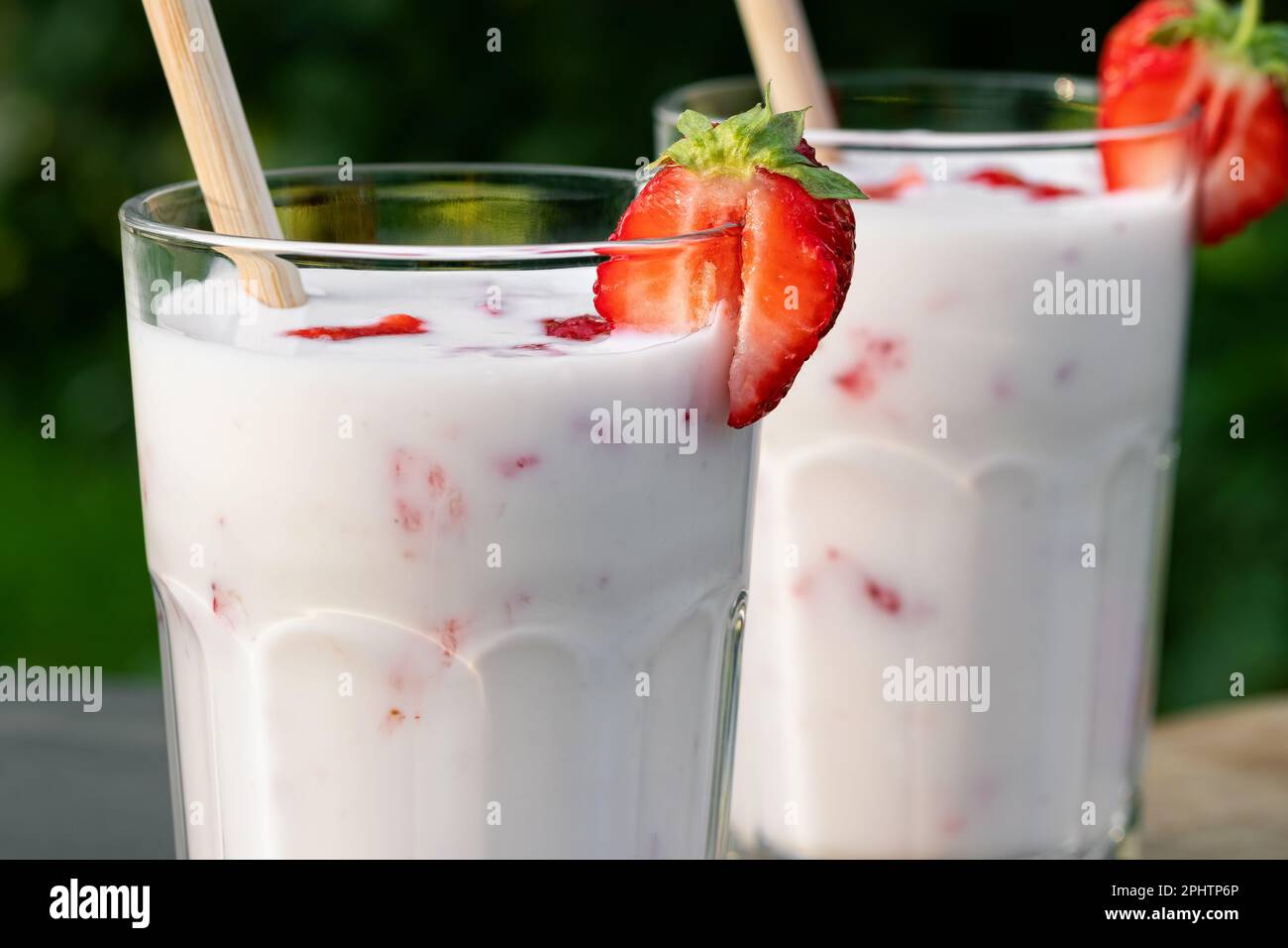 Erdbeer-Smoothie in zwei Glasgläsern und frische Erdbeeren auf einem Holztisch im Hof, Nahaufnahme. Stockfoto