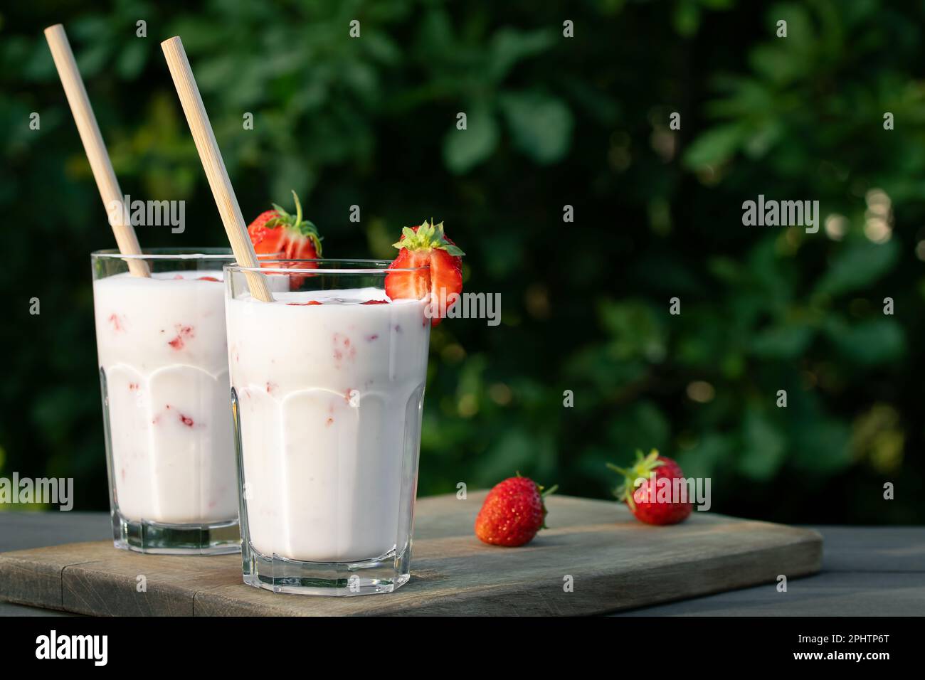 ErdbeerSmoothie in zwei Glasgläsern und frische Erdbeeren auf einem Holztisch im Hof, Kopierraum. Stockfoto