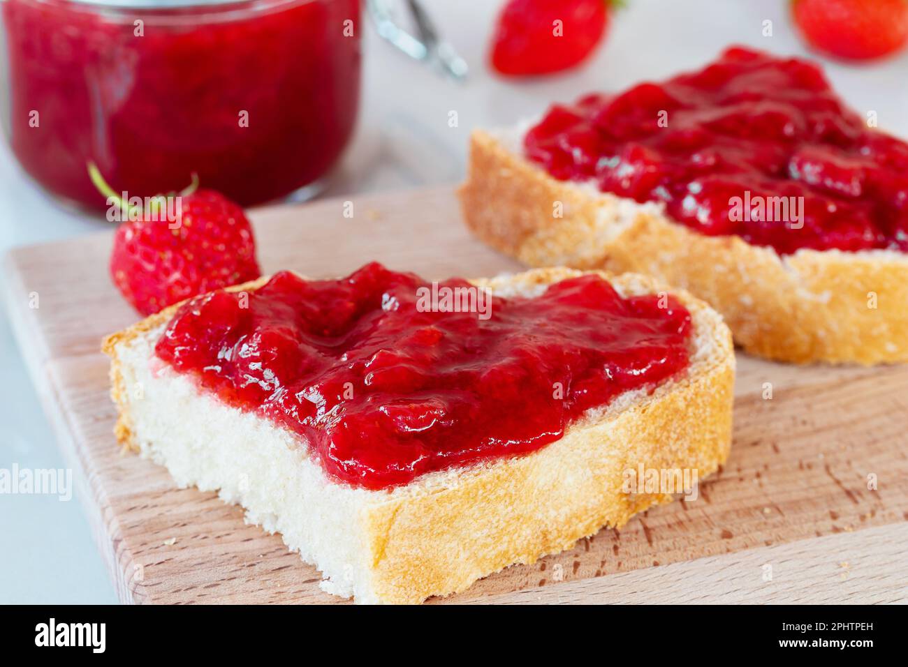 Weizenbrot mit aufgestrichener Erdbeermarmelade auf dem Tisch. Stockfoto