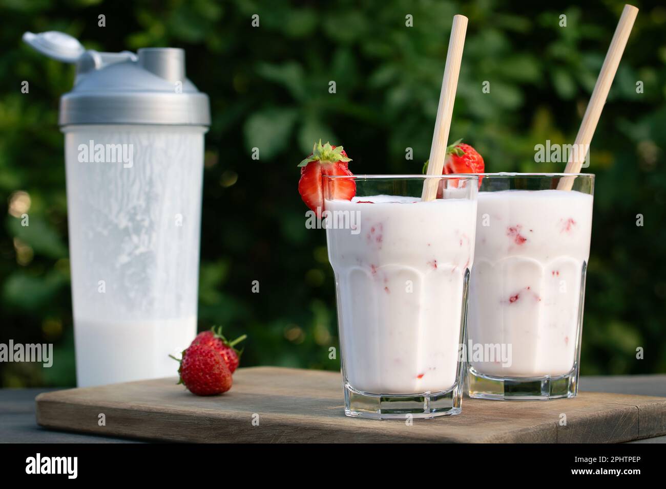 Proteinshake aus Joghurt und Erdbeeren in einem Schüttler und zwei Glasgläser auf einem Holztisch. Stockfoto