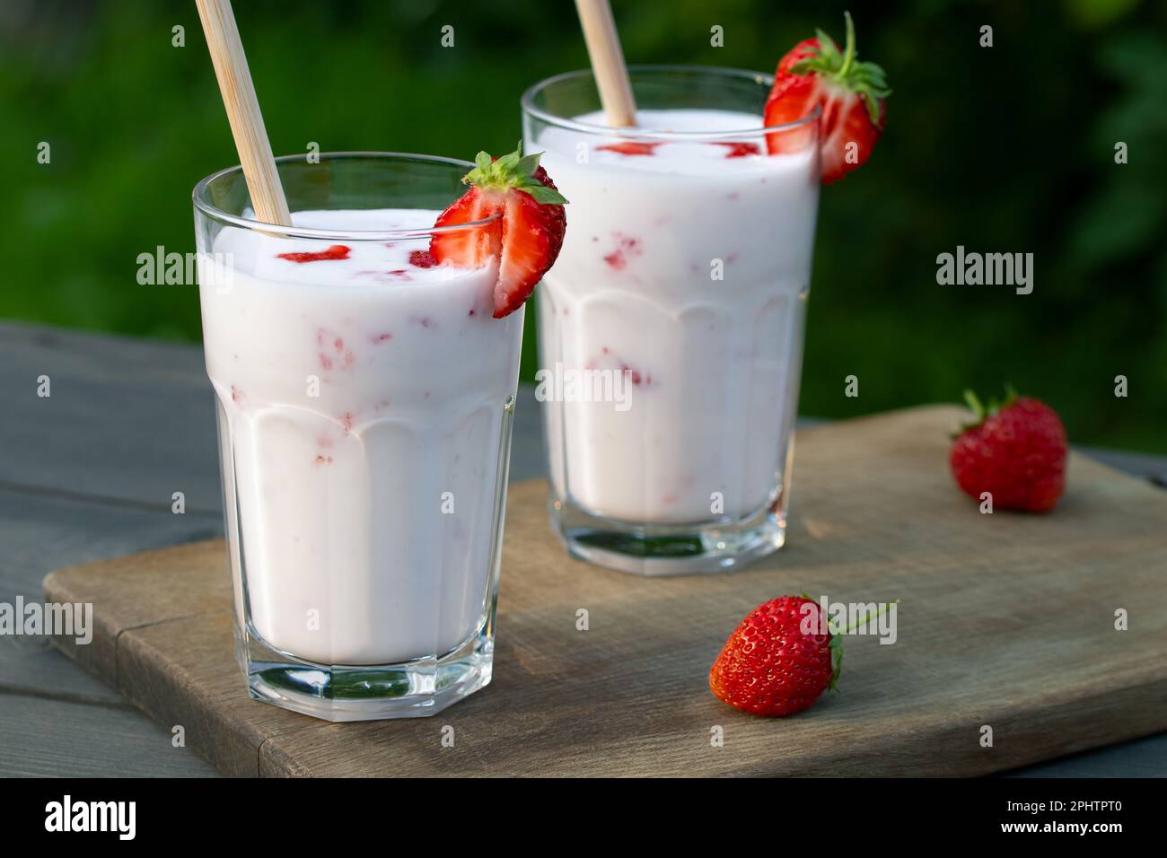 ErdbeerSmoothie in zwei Glasgläsern und frische Erdbeeren auf einem Holztisch im Hof. Stockfoto