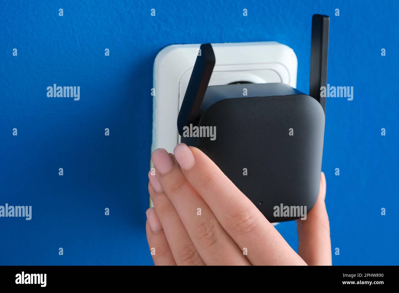 Frau, die den schwarzen WLAN-Repeater in die Steckdose an der blauen Wand steckt Stockfoto
