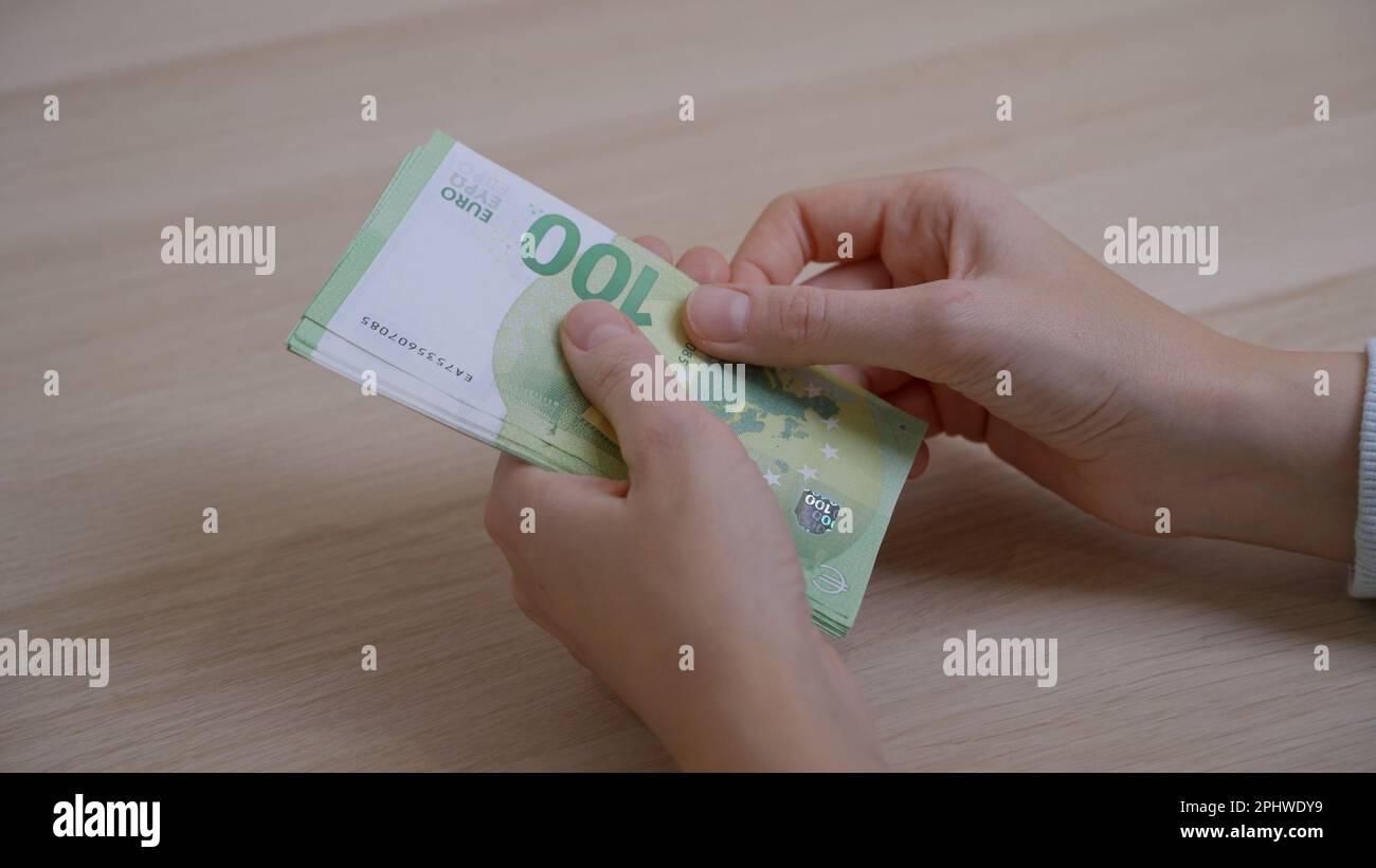 Frauenhände mit einer ordentlichen Maniküre zählen langsam Papiergeld mit einer Stückelung von 100 Euro über dem Tisch und kombinieren dann die Scheine zu einem P. Stockfoto