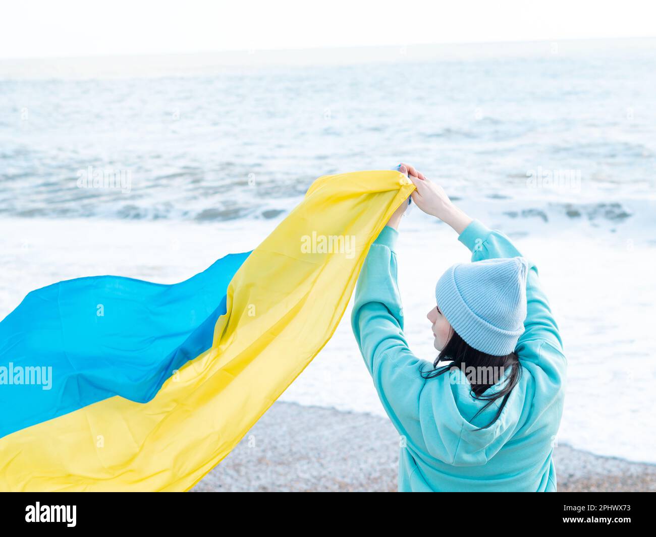 Braune Frau in blauem Hoodie und blauem Hut mit ukrainischer Nationalflagge, patriotisches Konzept Stockfoto