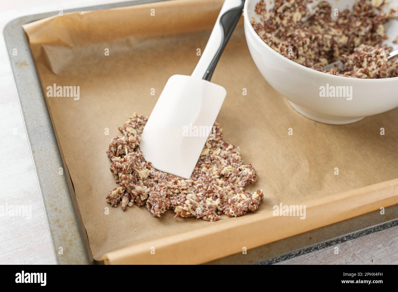 Teig aus Leinsamen und Haferflocken wird auf einem Tablett mit Backpapier verteilt, um gesunde knusprige Backwaren, ausgewählten Fokus und eine geringe Tiefe von Fi herzustellen Stockfoto