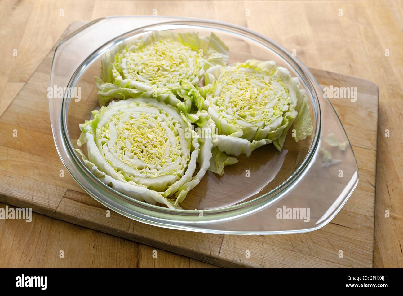 Scheiben rohen Chinakohls oder napakohls in einem Glasauflauf auf einem hölzernen Küchenbrett, zubereitet zum Backen im Ofen, kreative vegetarische Küche, Polizist Stockfoto