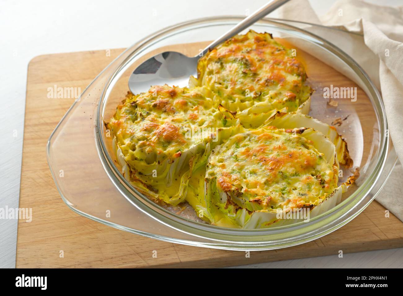 Gebackene Scheiben Chinakohl oder napakohl in einem Glasauflauf auf einem hölzernen Küchenbrett, kreatives vegetarisches Gericht, Kopierraum, ausgewählter Fokus, schmales d Stockfoto