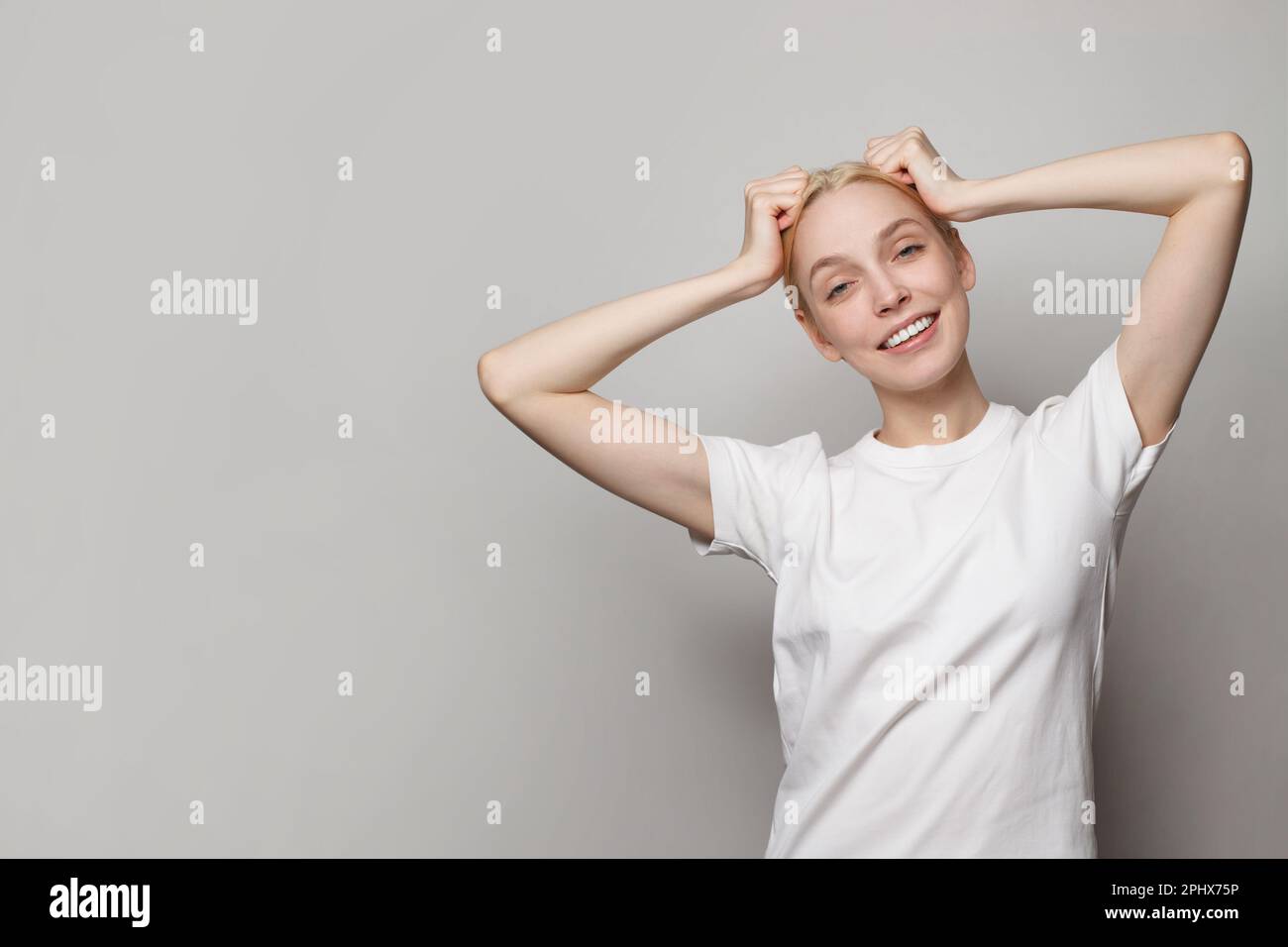 Fröhliche junge Frau, die ein weißes leeres T-Shirt trägt und auf grauem Studiohintergrund posiert Stockfoto