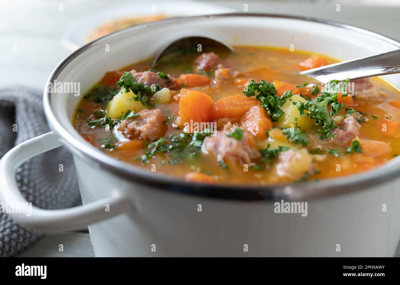 Eintopf mit Karotten, Kartoffeln und geräuchertem Schweinefleisch in einem weißen Emaille-Topf. Stockfoto