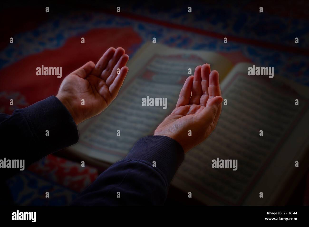 Islamisches Foto. Gebetender muslimischer Mann mit erhobenen Händen. Der Heilige Koran im Hintergrund. Ramadan oder islamisches Konzeptfoto. Selektiver Fokus. Stockfoto