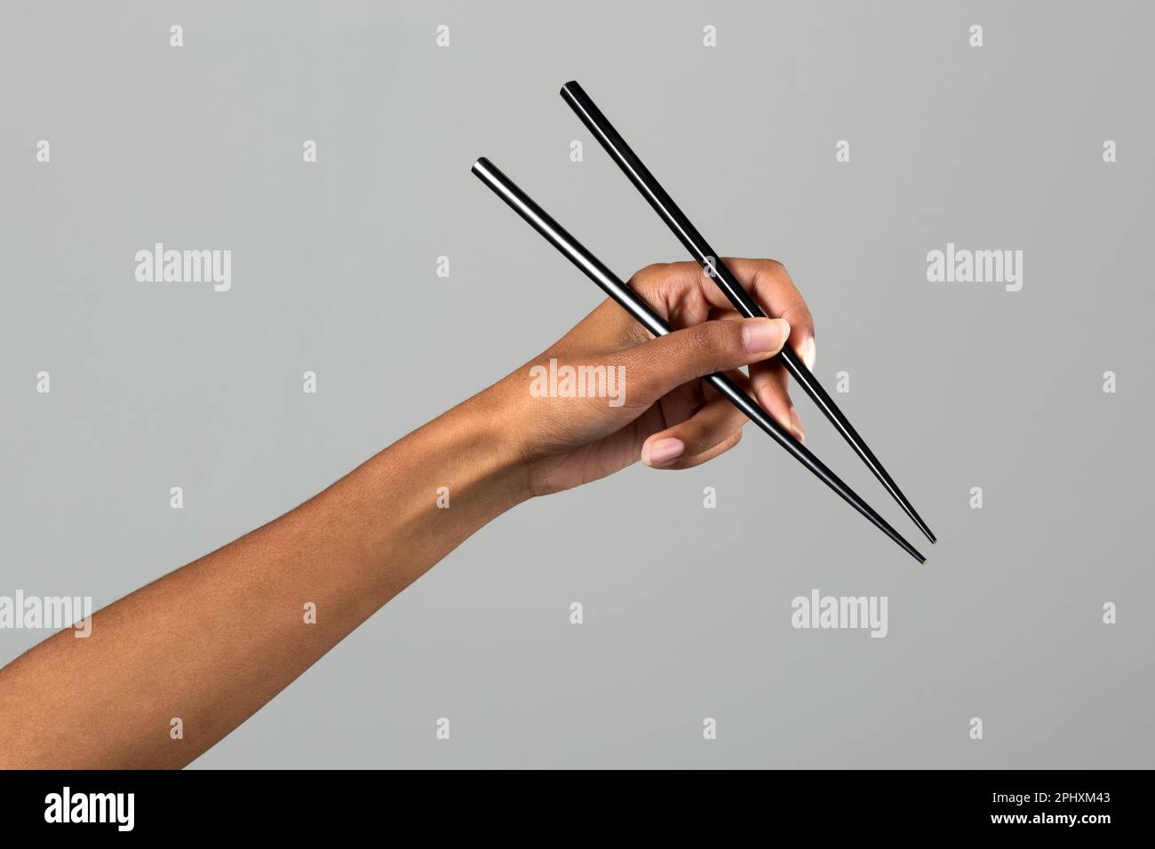 Nicht erkennbare schwarze weibliche Hand, die chinesische Essstäbchen vor grauem Hintergrund in einem hellen Studio hält Stockfoto