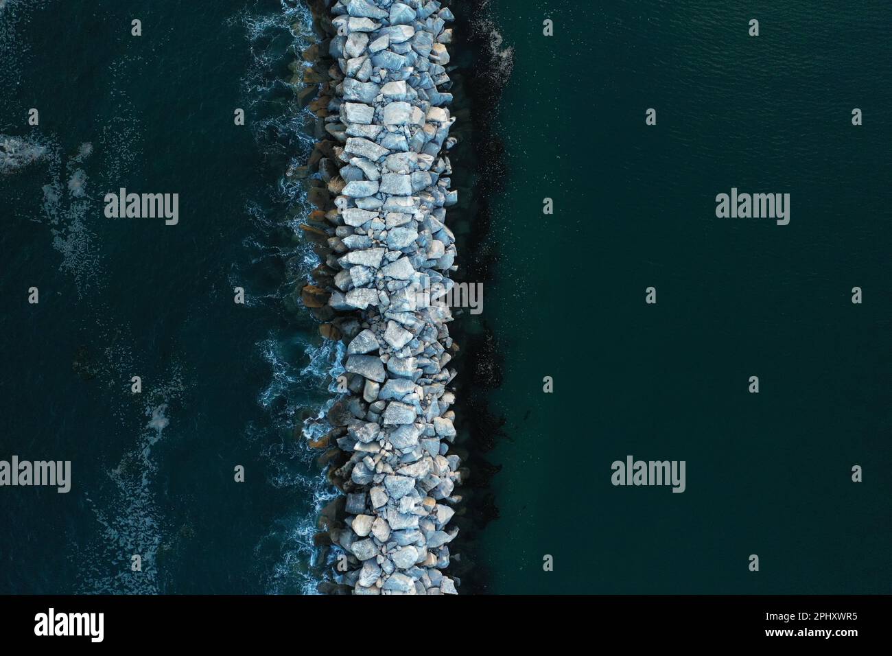 Ein malerischer Blick auf eine zerklüftete Felsformation, die aus dem kristallklaren Wasser des Meeres ragt, mit der Sonne im Hintergrund Stockfoto