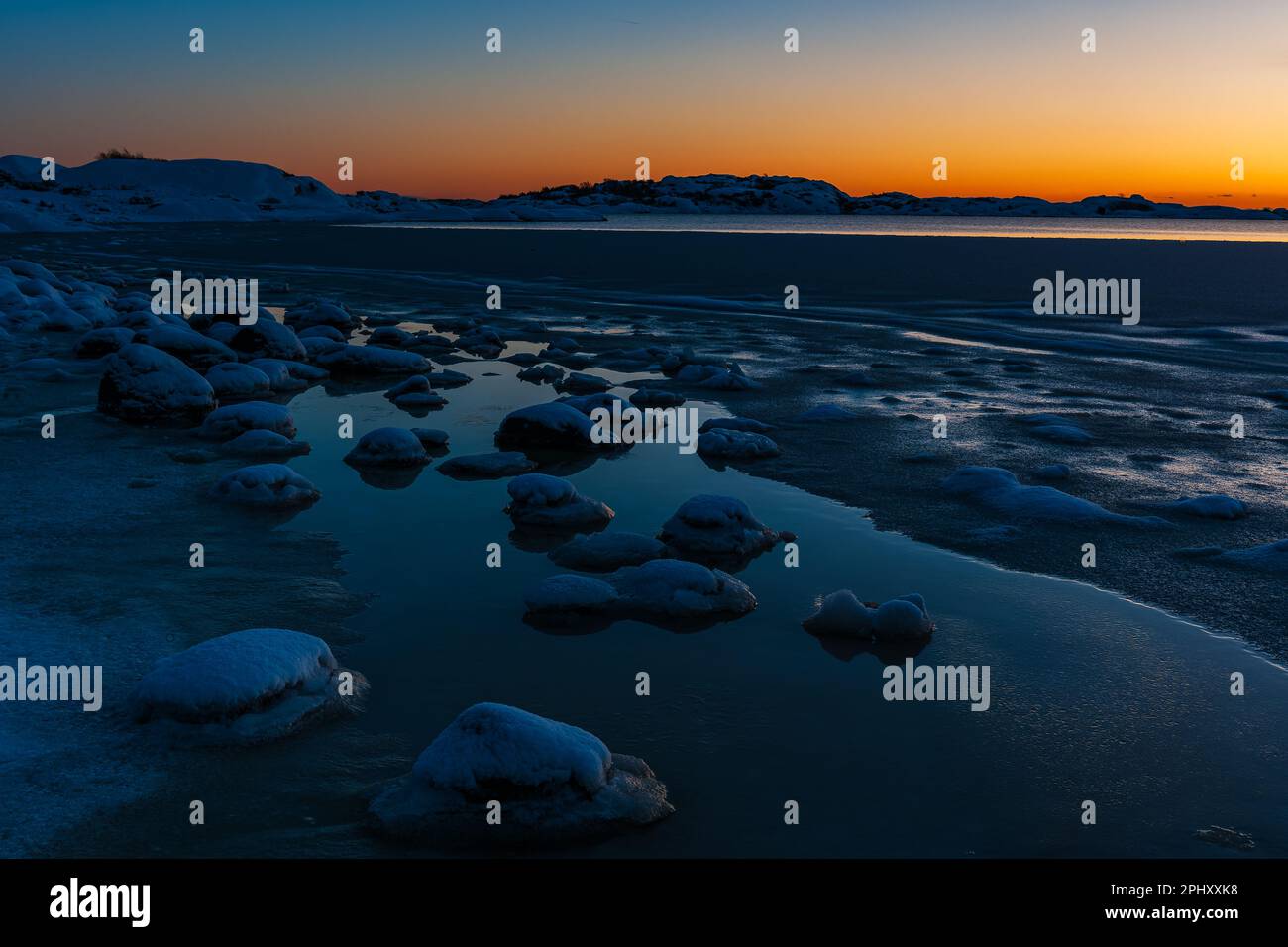 Eine wunderschöne und friedliche Morgendämmerung entlang der schwedischen Küste, die ein ruhiges gefrorenes Meer an einem orangefarbenen Horizont reflektiert. Stockfoto