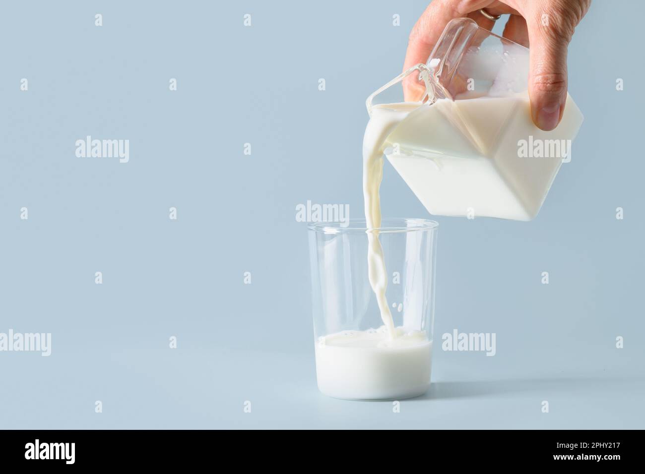 Gießen Sie organische Milch in Glas auf blauem Hintergrund. Speicherplatz kopieren. Weltmilchtag. Stockfoto