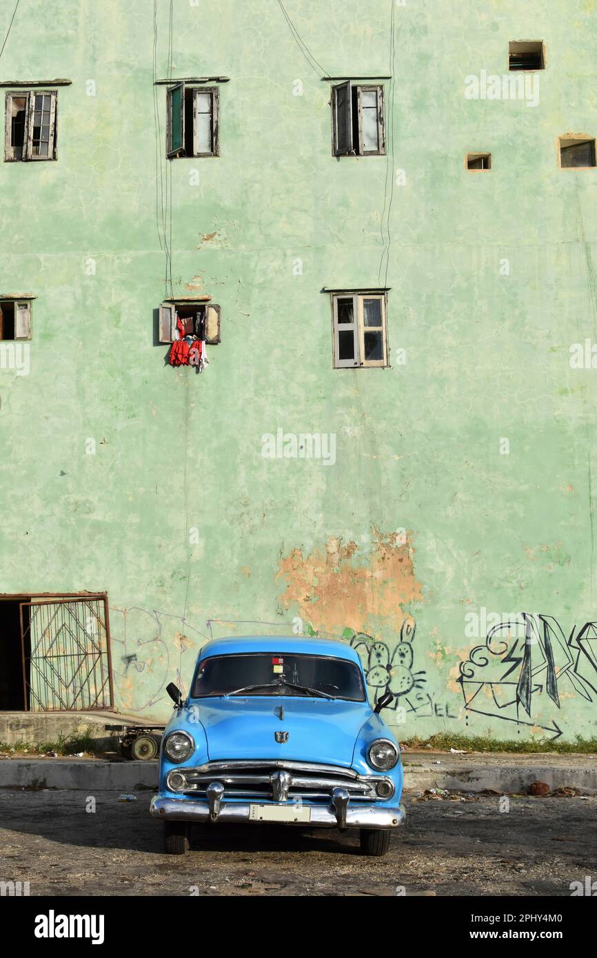 Ein blauer Oldtimer parkt vor dem grünen Gebäude. Die Fenster dieses Hauses in verschiedenen Dimensionen und die Graffiti spiegeln den Charme des wider Stockfoto