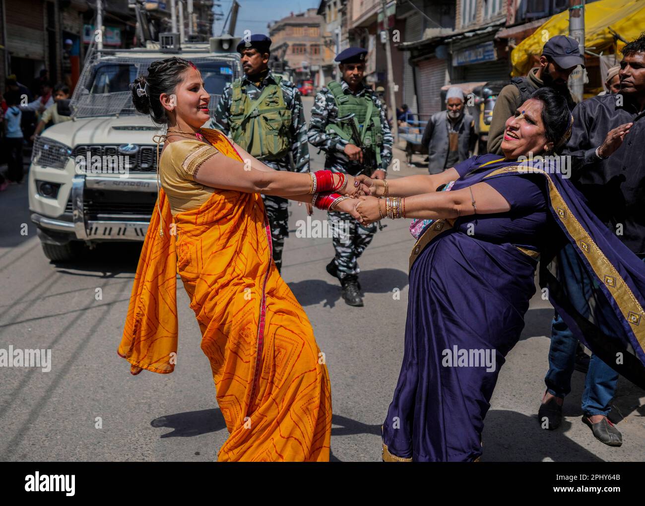 Kashmiri Hindu women dance as security men patrol during a procession