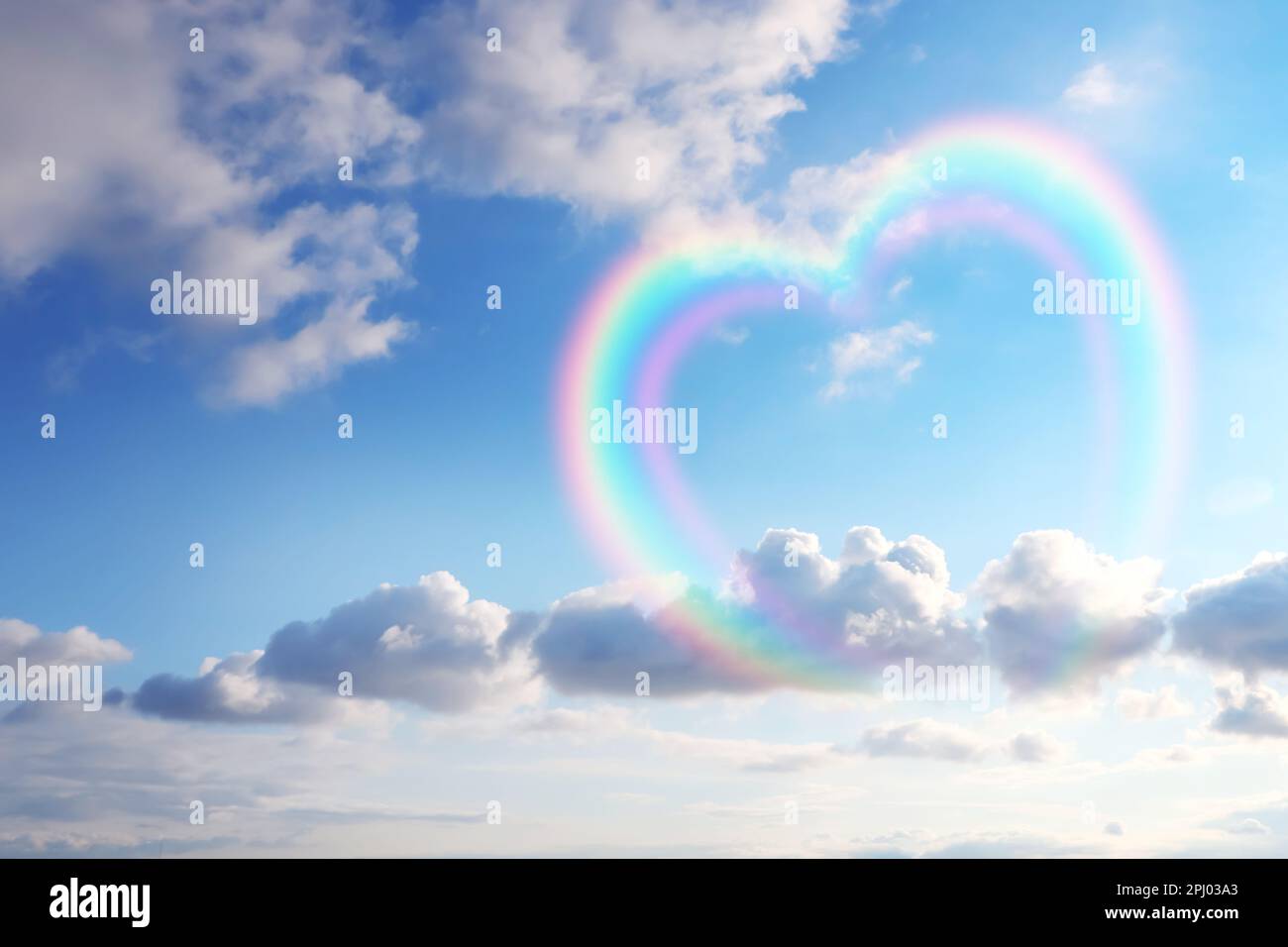 Wunderschöner Blick auf herzförmigen Regenbogen und weiße Wolken am blauen Himmel an sonnigen Tagen Stockfoto