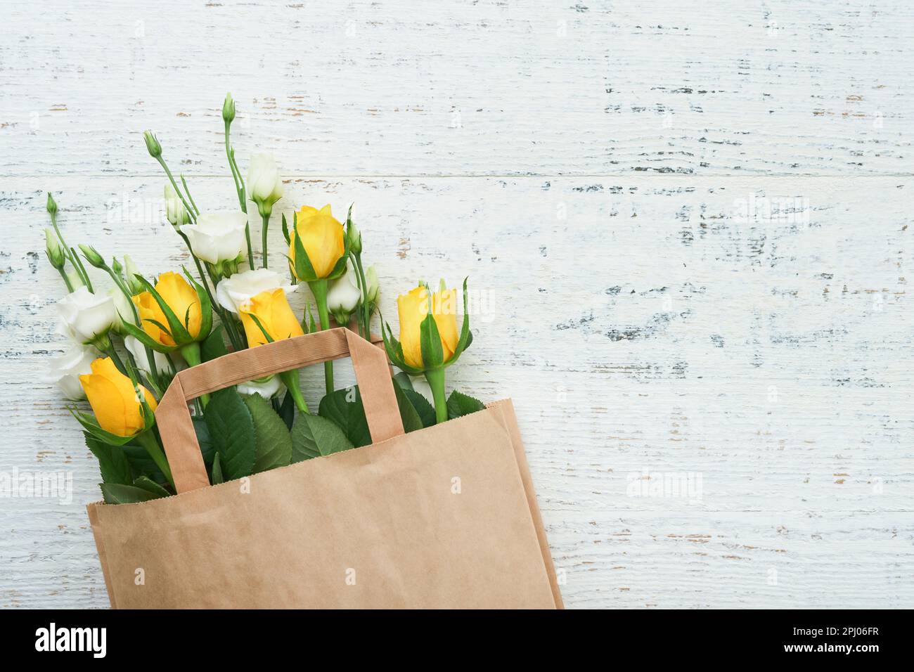 Osterkonzept. Strauß frischer weißer und gelber Rosen in einer Papiertüte auf altem weißem Holzhintergrund. Pessover-Pesah-Festungskonzept. Konzept von Mo Stockfoto