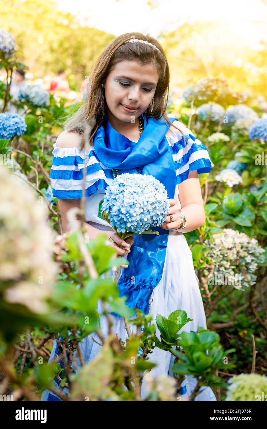 Schöne Nicaraguanerin in Nationalkostüm, die Blumen in einem Kinderzimmer hält. Porträt eines Mädchens in traditionellem zentralamerikanischen Folkloregeschmuck Stockfoto