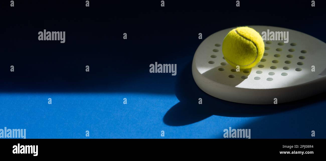 Weißer professioneller Paddle-Tennisschläger und gelber Ball mit natürlicher Beleuchtung auf blauem Hintergrund. Horizontales Sportposter, Grußkarten, Kopf Stockfoto