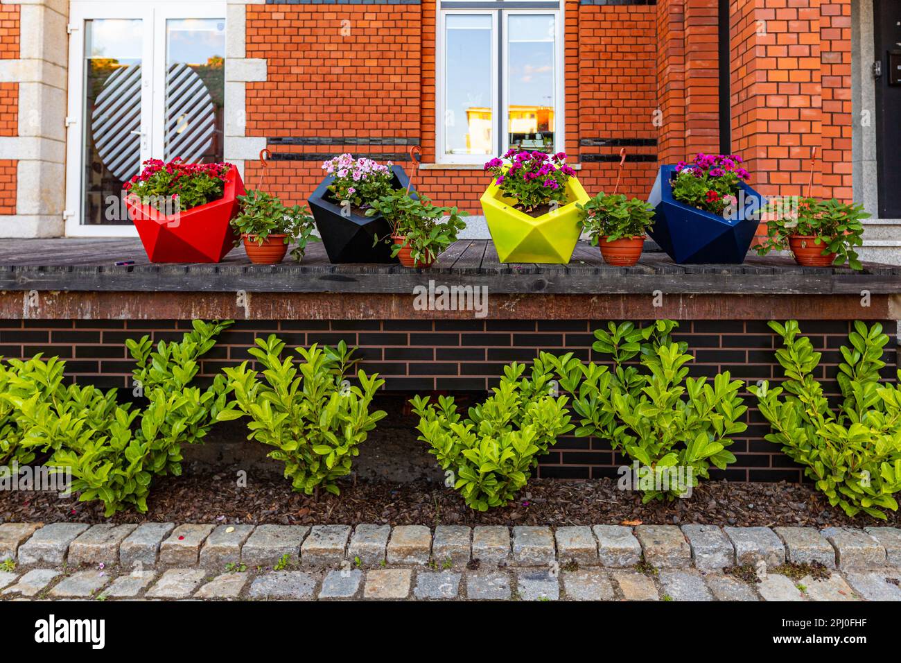 Breslau, Polen - Juni 2022: Vier große bunten Pflanzmaschinen und vier kleinere voller Blumen stehen vor einem modernen Bürogebäude aus rotem Ziegelstein Stockfoto