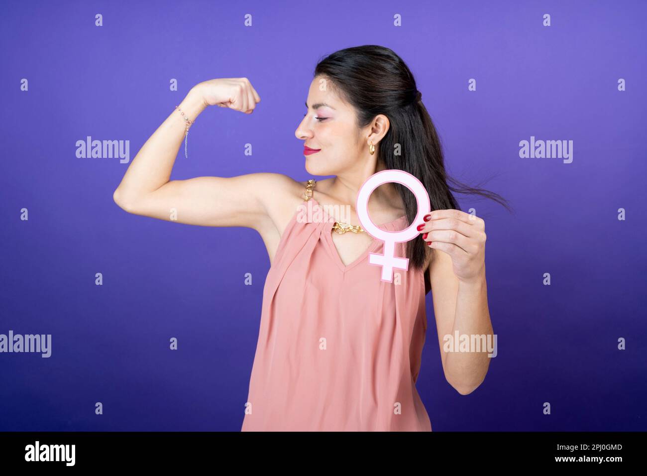 Eine Frau, die ihre Stärke am Arm zeigt und das feministische Symbol in der Hand hält, auf einem isolierten Hintergrund Stockfoto