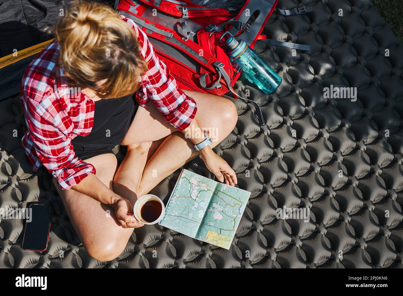 Frau, die die nächste Reise plant, während sie mit Karte im Zelt sitzt. Frau, die sich im Zelt während der Sommerferien beim Camping entspannt. Verbringen Sie aktiv Urlaub im Freien Stockfoto