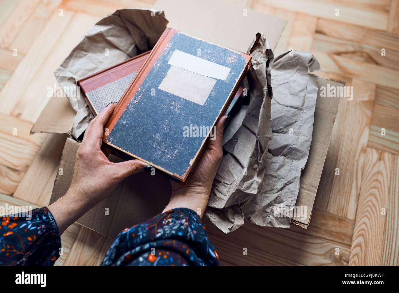 Eine Frau, die Bücher aus dem Karton nimmt. Paket wird ausgepackt. Weibliche Hände mit Büchern Stockfoto