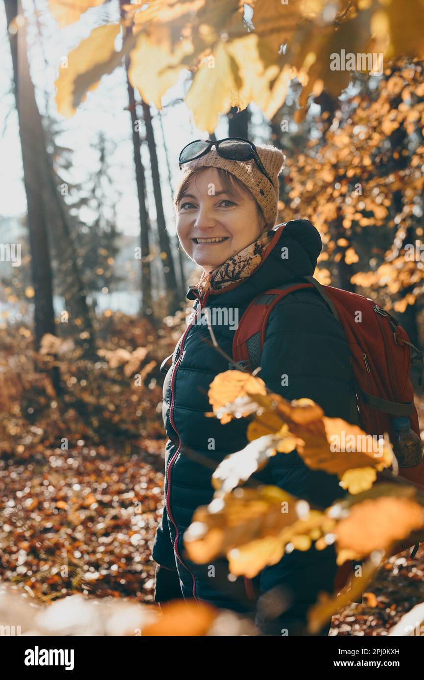 Frau mit Rucksack, die an einem sonnigen Herbsttag in einem Wald umherwandert. Vorderansicht einer mittelalterlichen aktiven Frau, die aktiv Freizeit auf dem Waldweg verbringt Stockfoto