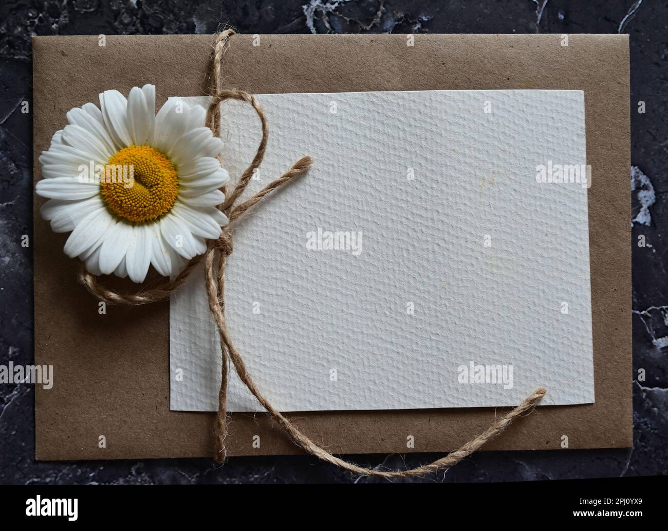 Eine leere Grußkarte mit einem braunen Umschlag und einer weißen Blume für die mutter auf einem Holztisch im Vintage-Stil und mit Vignetten Stockfoto