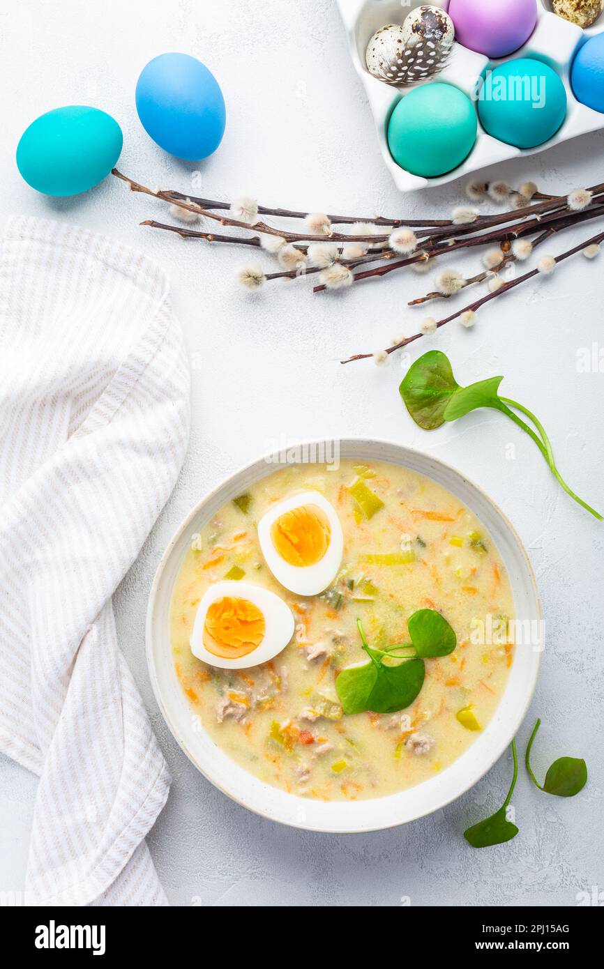 Traditionelle polnische Sauersuppe Zurek mit Rochenmehl, g und Gemüse auf dem Küchentisch mit Osterdekoration Stockfoto