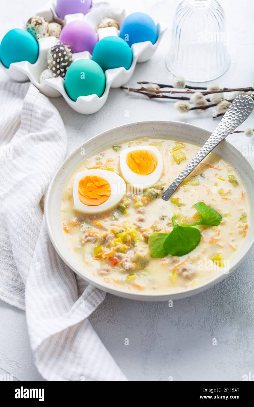 Traditionelle polnische Sauersuppe Zurek mit Rochenmehl, g und Gemüse auf dem Küchentisch mit Osterdekoration Stockfoto