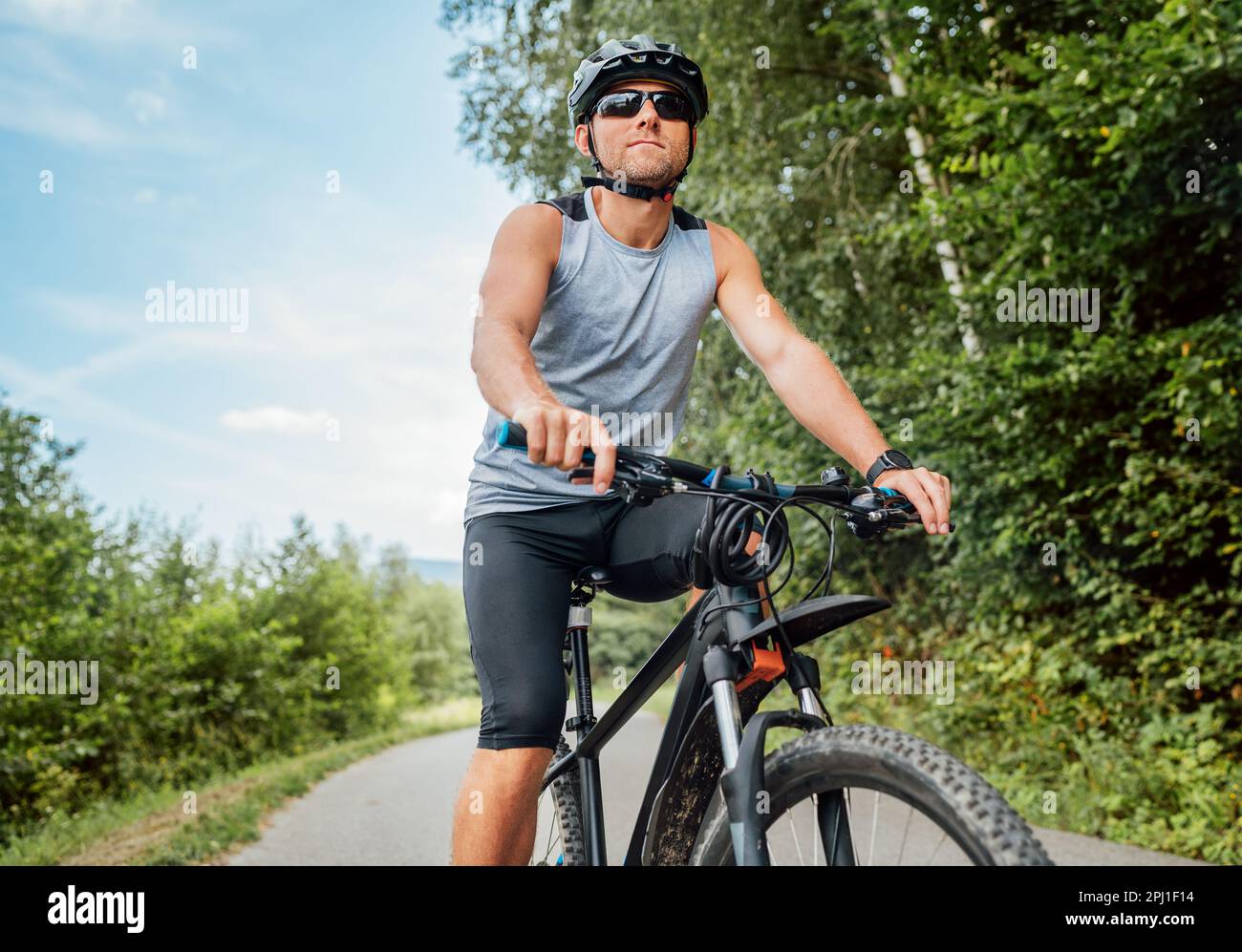 Porträt eines glücklichen Mannes in Radkleidung, Helm und Sonnenbrille, der auf einem Fahrrad auf dem Radweg außerhalb der Stadt fährt. Das Konzept des aktiven, sportlichen Menschen Stockfoto